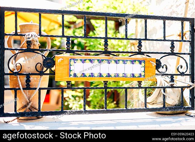 Blank sign on a forged metal fence against the background of clay jugs. High quality photo