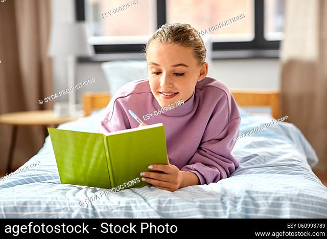 smiling girl writing to diary lying on bed at home
