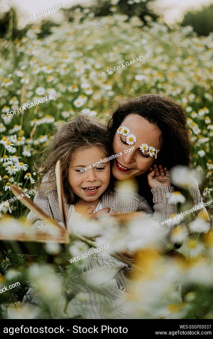 Mother sitting with daughter amidst flowering plants at field