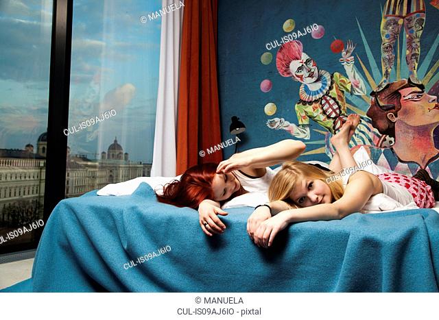 Two sleepy young women lying on hotel bed