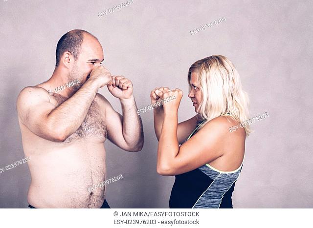 Shirtless corpulent man and woman standing against each other ready to fight
