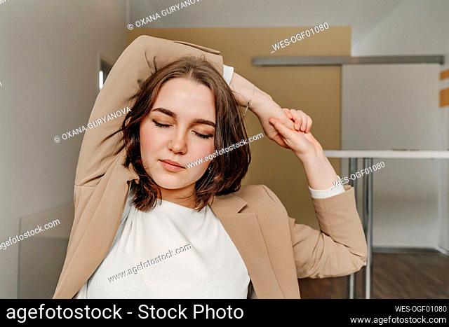 Tired female professional with eyes closed stretching hands sitting in office