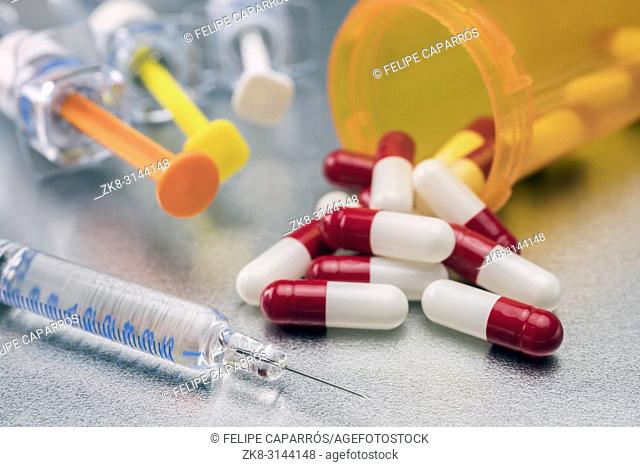 Syringes of several types along with bottle of white and red pills, conceptual image