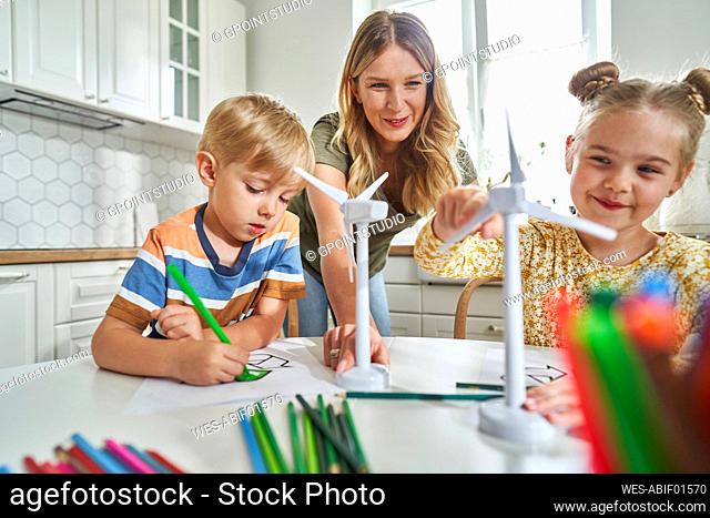 Mother teaching children about wind turbine model at table