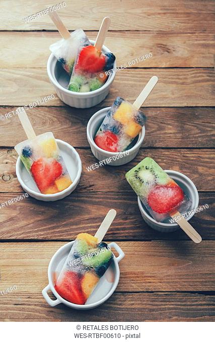Bowls of fruit ice lollies with fresh fruits on white ground