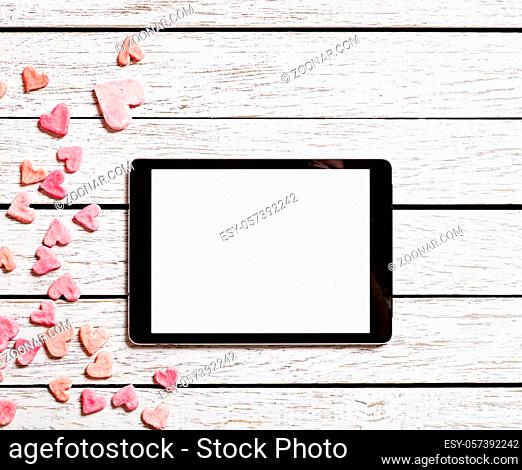 Digital tablet on white wood table with heap of small hearts