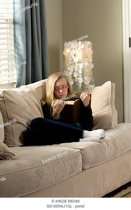 Pre adolescent girl reclining on sofa reading book