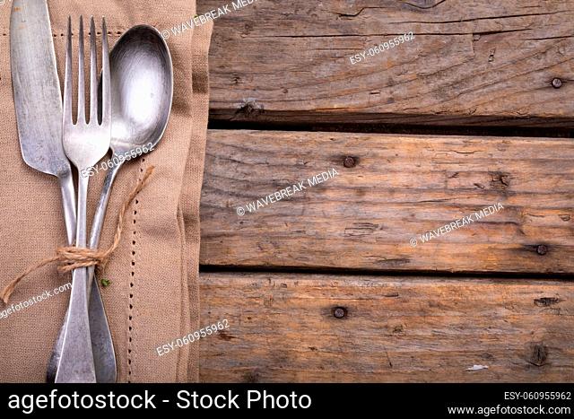 Close up of cutlery set over a napkin on wooden surface