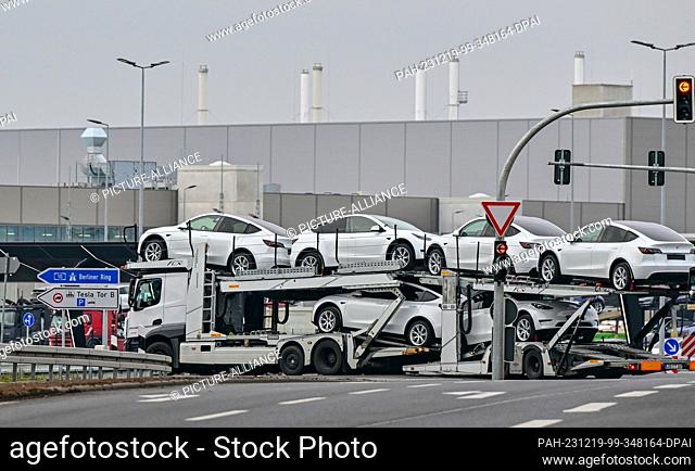 PRODUCTION - 18 December 2023, Brandenburg, Grünheide: A car transporter has loaded Tesla Model Y electric vehicles and drives past the Tesla Gigafactory...
