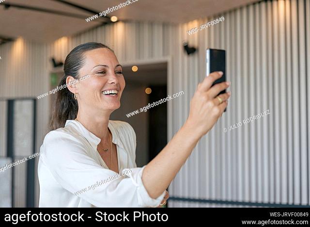 Cheerful mature businesswoman on video call through smart phone in lobby
