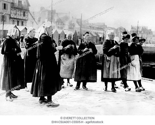 Wearing the unique costumes of Brittany, France, wives knits as they await the return of their fishermen husbands. Oct. 1926