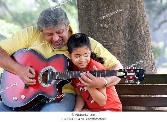 Grandfather teaching his granddaughter to play the guitar