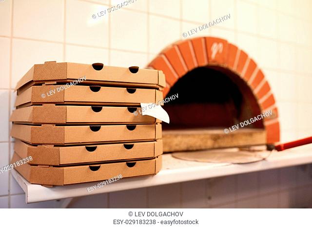fast food, italian kitchen, takeaway, delivery and eating concept - close up of pizza in paper box on table at pizzeria oven