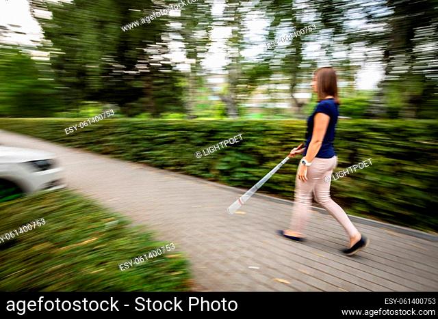 Blind woman walking on city streets, using her white cane