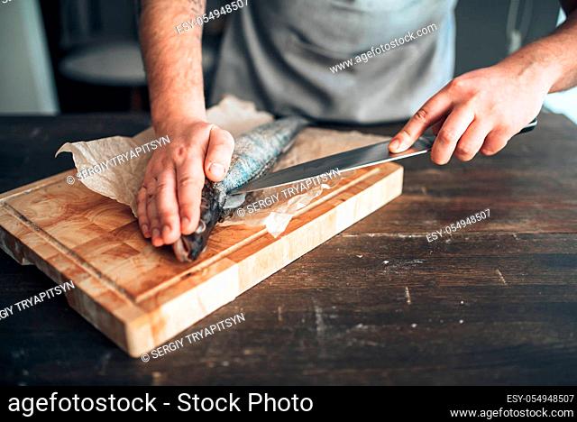 Male chef hands with knife cut up raw fish on cutting board