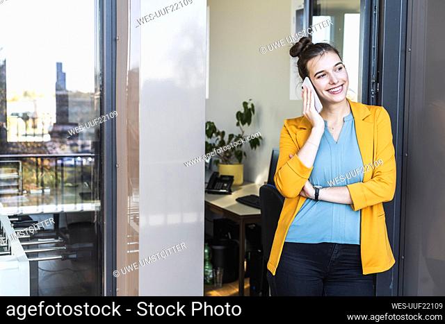 Businesswoman talking on mobile phone while standing at door in office