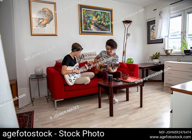 Young people playing guitars on sofa