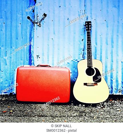 A guitar and old suitcase sit in front of an old shed