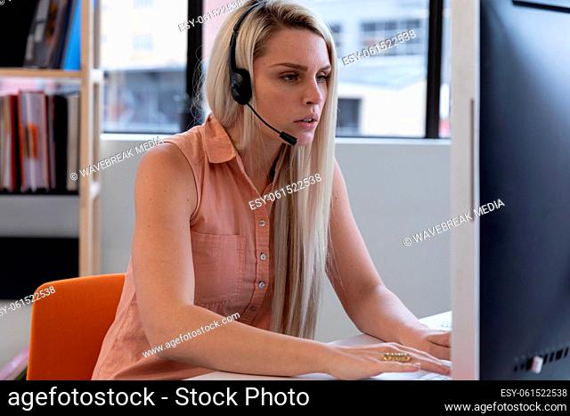 Caucasian woman wearing phone headset using computer in modern office