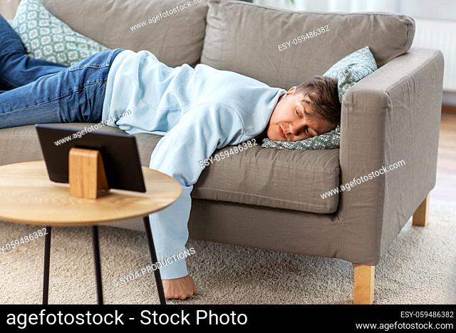 bored man with tablet pc lying on sofa at home