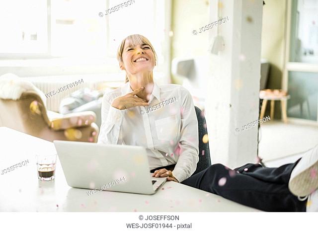 Confetti falling on businesswoman with laptop in office