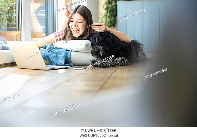 Happy young woman with dog lying at the window at home shopping online