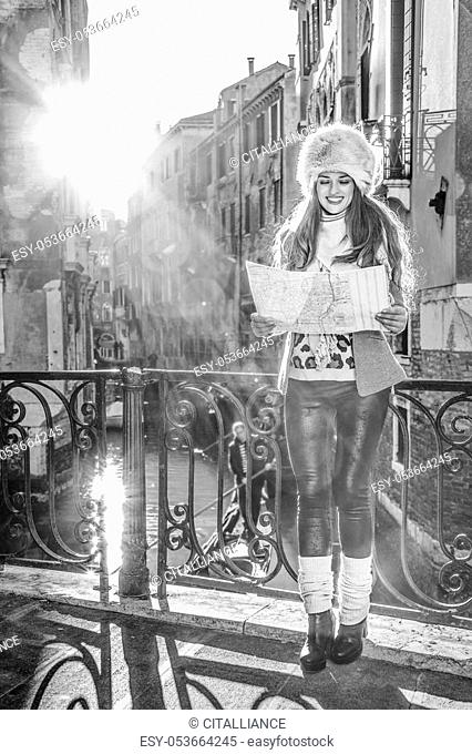 Venice. Off the Beaten Path. Full length portrait of smiling young tourist woman in fur hat in Venice, Italy in the winter looking at the map