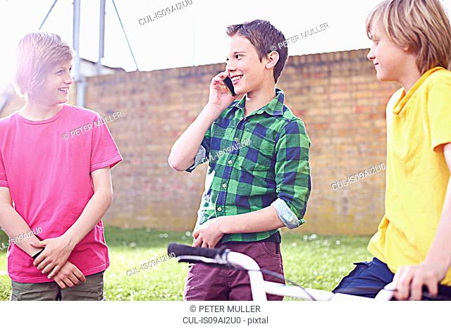 Boy using cell phone with two friends