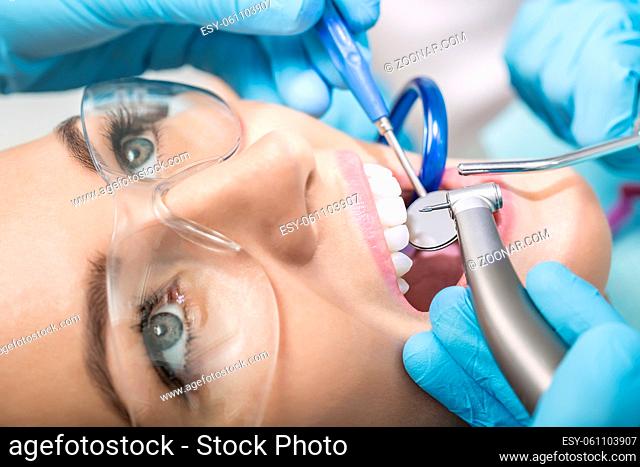 Macro photo of the teeth treatment in the dentist's office. Girl with open mouth in a protective glasses, hands in blue medical gloves with dental instruments...