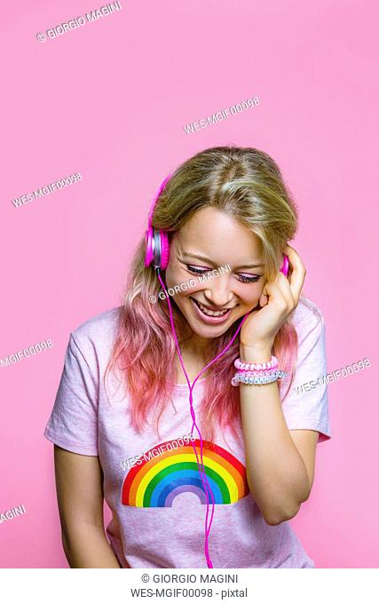 Portrait of young woman listening to music with headphones in front of pink background