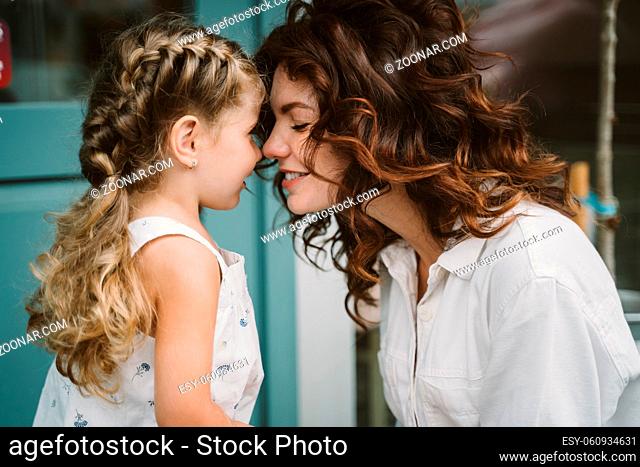 Portrait of little daughter kissing her beautiful happy mother outdoors