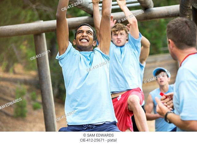 Determined men swinging on monkey bars on boot camp obstacle course
