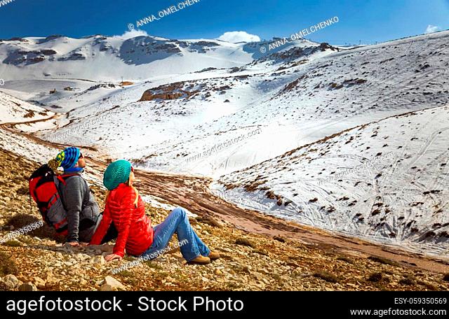 Happy Young Couple Sitting and Resting in the Mountains at Base Camp. Enjoying Adventure Hike in the beautiful Snowy Mountains