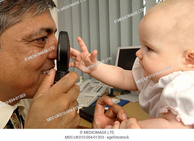 A GP using an ophthalmoscope to examine the health of a baby's retina and vitreous humour