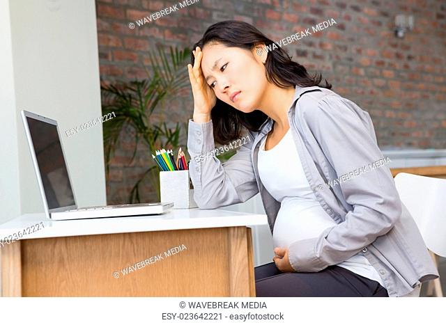 Suffering pregnant woman sitting at desk