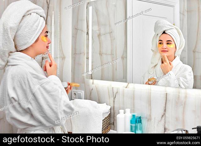 beautiful woman with eye patches in white bathrobes in front of mirror in bathroom