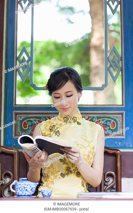 Young woman with cheongsam reading a book