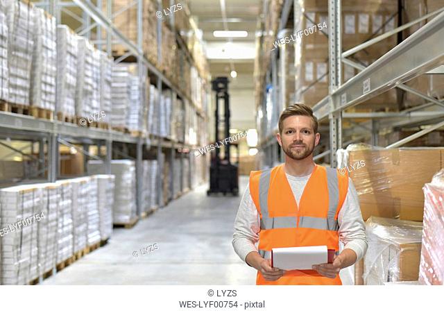 Portrait of confident man in factory hall wearing safety vest holding clipboard