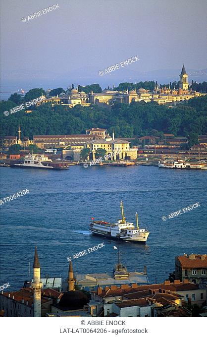 View of Topkapi palace on wooded hill from the Golden Horn sea channel. Ferry boats. Sunset
