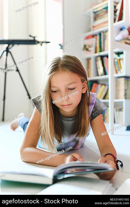 Girl reading book lying at home