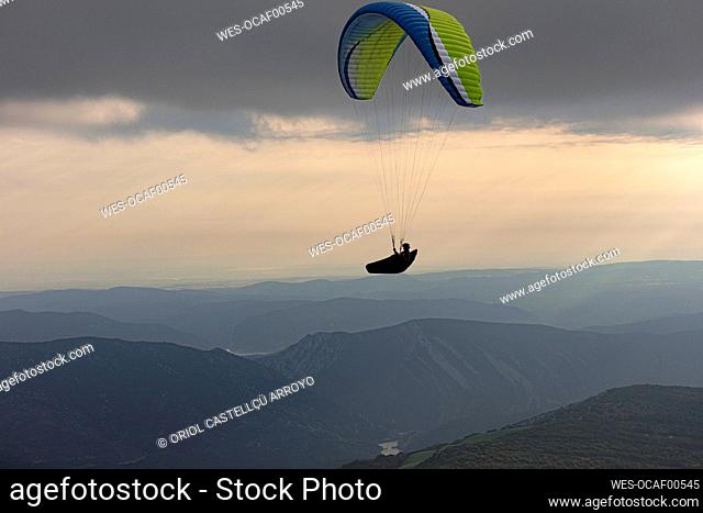 Aerial view of male paraglider soaring above mountains at dusk