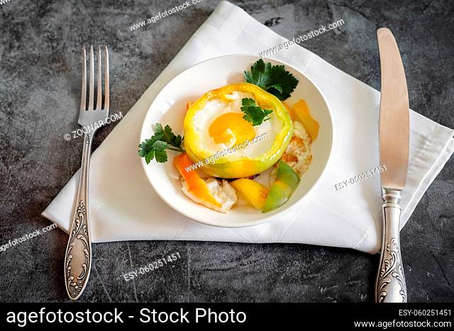 On the table on a plate is an oven-baked bell pepper with an egg inside the pepper. There are Cutlery on a napkin nearby. Top view with space to copy