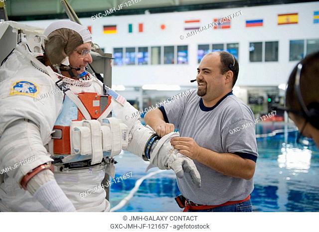 Astronaut T.J. Creamer, Expedition 2223 flight engineer, gets help in the donning of a training version of his Extravehicular Mobility Unit (EMU) spacesuit in...