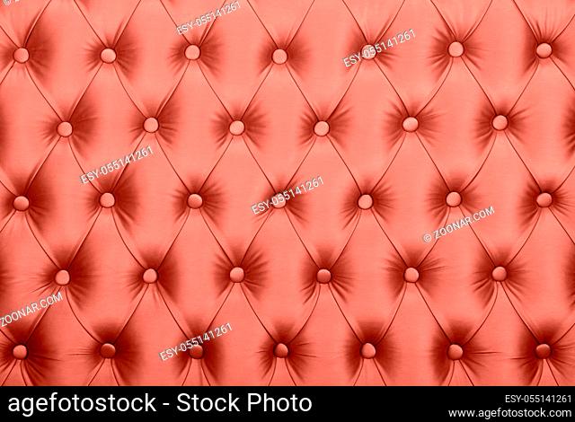 Coral toned pink leather capitone textile background, retro Chesterfield style checkered soft tufted fabric furniture decoration with buttons, close up