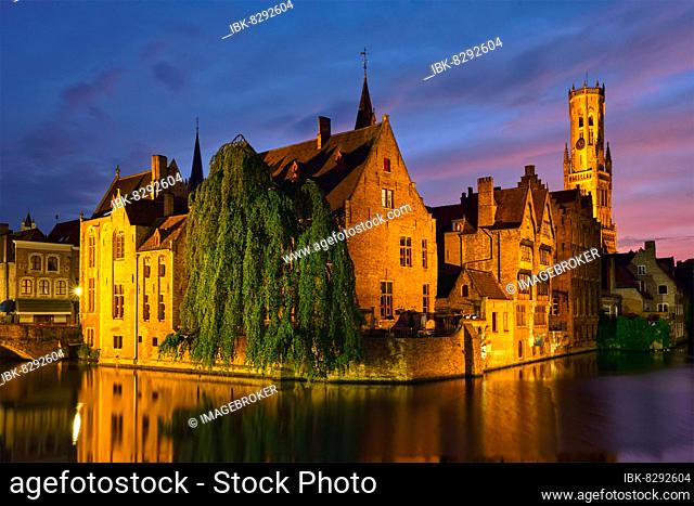 Famous view of Bruges tourist landmark attraction, Rozenhoedkaai canal with Belfry and old houses along canal with tree in the night