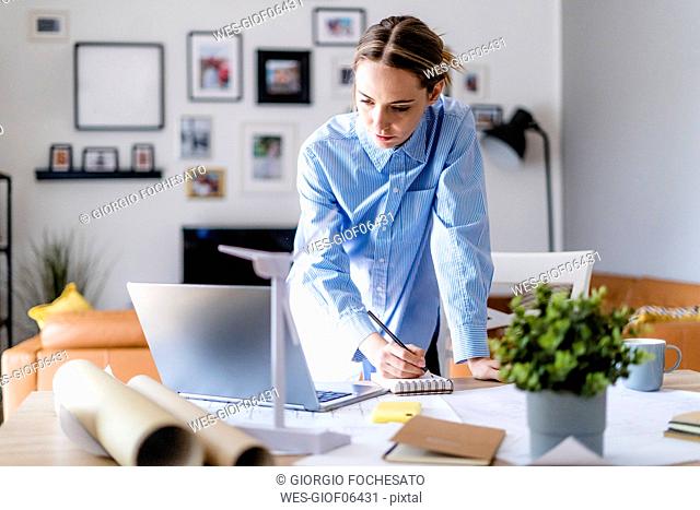 Woman in office taking notes with laptop and wind turbine model on table