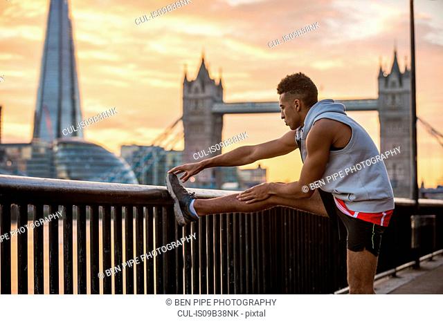 Man stretching against railing, Tower Bridge and The Shard in background, Wapping, London, UK