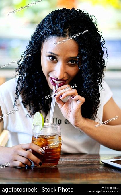 Portrait of smiling young woman drinking while sitting at table in restaurant