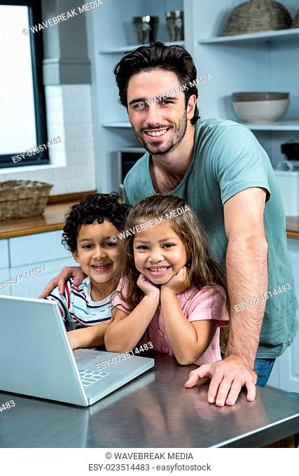 Smiling father using laptop with his children in kitchen