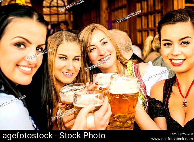 Girls in traditional Dirndl dresses are drinking beer and having fun at the Oktoberfest, mixed races: One Asian, one Russian, two Caucasian girls